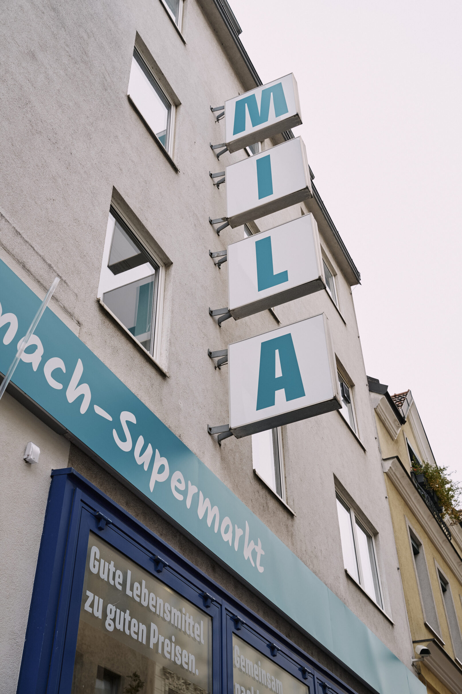 Ein Foto der Außenfassade des MILA Mitmach-Supermarktes, Beschidlerung und Leuchtschriftzug sind angeshcnitten sichtbar.